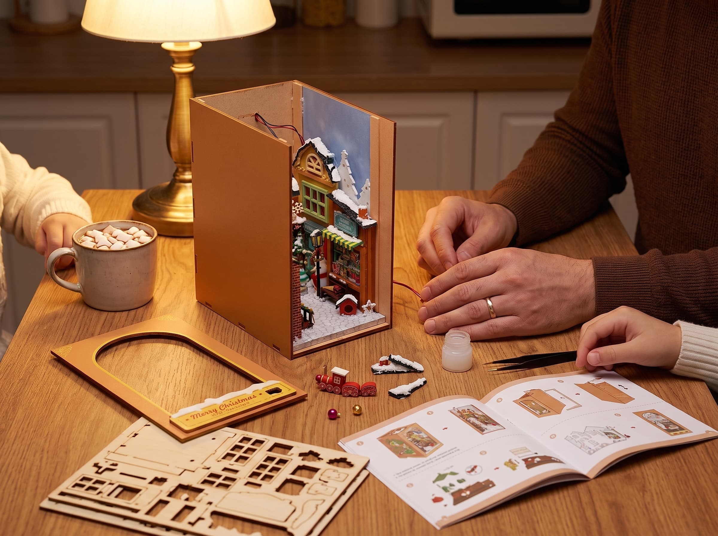 Two pairs of hands assembling the Christmas Village book nook at a warm kitchen table